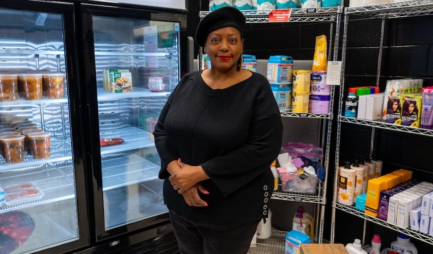 A woman standing in a pantry with food on shelves smiling.