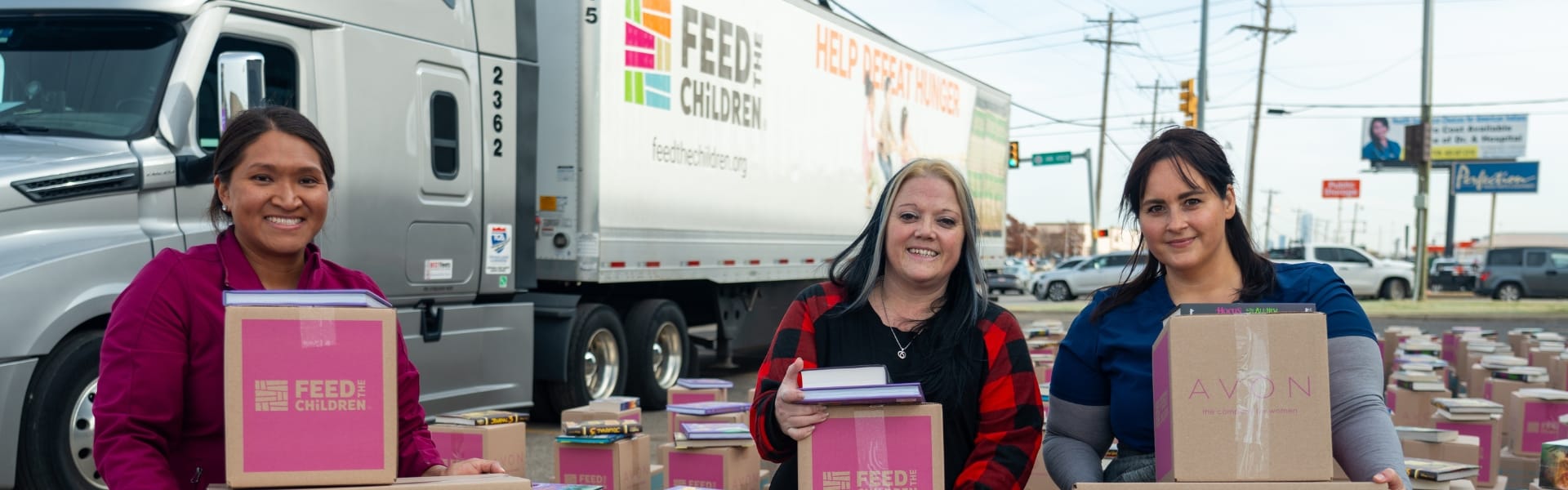 Three women standing with boxes at an outdoor event