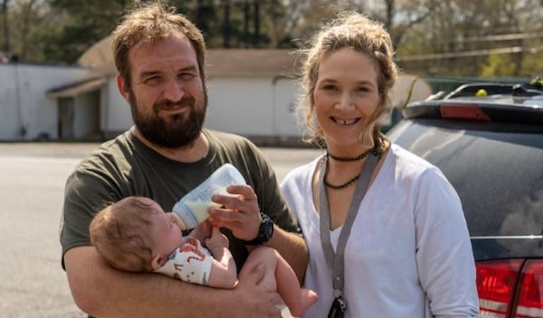 Two people holding and feeding a baby outdoors