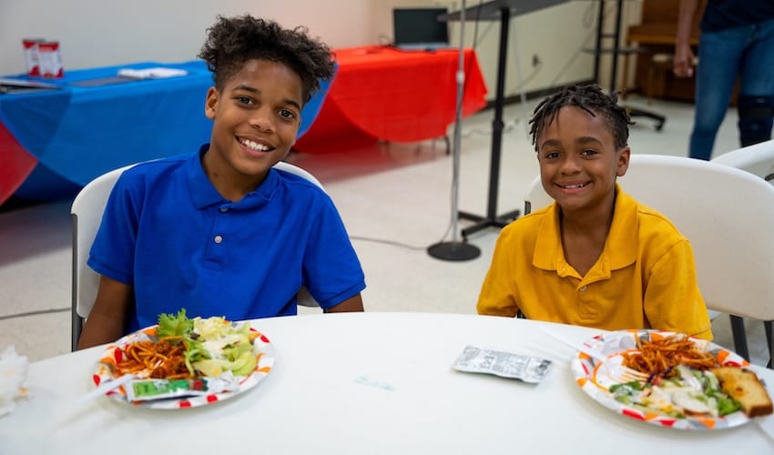 Two boys sitting at a table with food on plates in front of them.