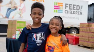 Two children hugging at an outdoor event with boxes